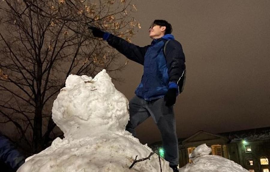 A college student standing on top of a snowman and pointing.