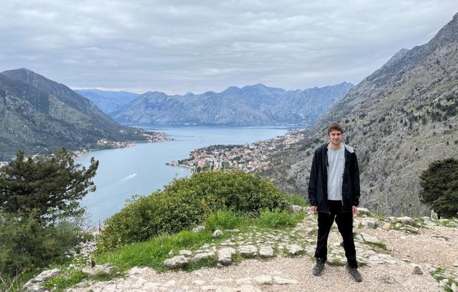 A college student standing in front of a lake and mountain view.
