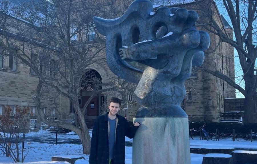 A college student standing with an abstract sculpture.